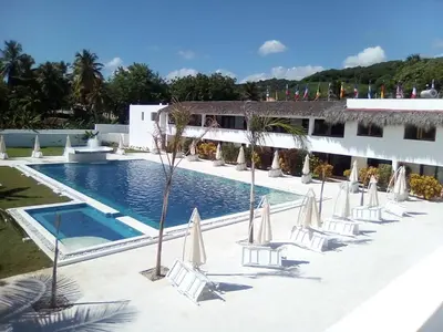 a pool with chairs and umbrellas in front of a building at Oasi Encantada - Beach Resort in Santa Cruz de Barahona