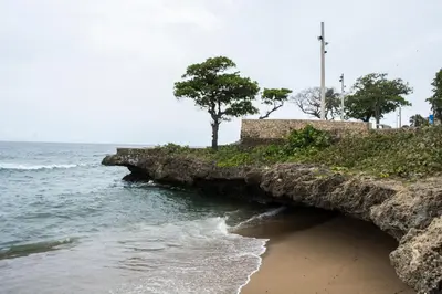 a rock wall next to the ocean with a beach at Malecon Rooms y Hotel in Santo Domingo