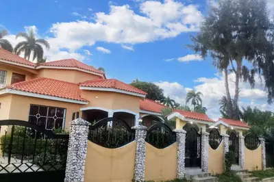 a fence in front of a house with palm trees at Elegant Villa in Nagua with Private Pool and Jacuzzi in Nagua