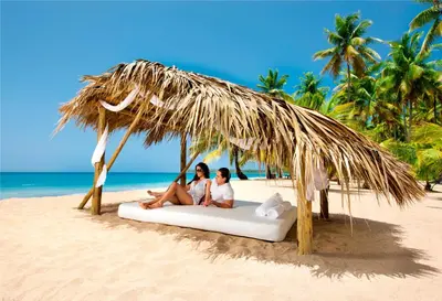 two women sitting on a beach under a straw umbrella at Sublime Samana in Las Terrenas