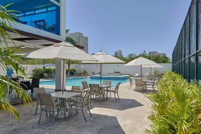a group of tables and chairs with umbrellas next to a pool at Elegante Aqua Marine Apartamento Juan Dolio in Juan Dolio