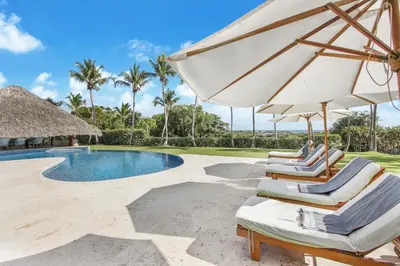 a group of chairs and an umbrella next to a swimming pool at Unique Villa with Ocean and River Views - Staff & Golf Carts in La Romana