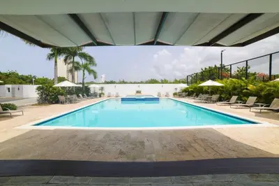 a large swimming pool with chairs and umbrellas at Blue Boat Lindo Apartamento en Playa Juan Dolio in Juan Pedro