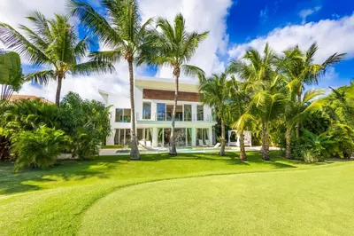 a house with palm trees in front of a yard at Luxury Rentals in Punta Cana - Exclusive Waterfall Villa with Private Pool, BBQ, Maid, Golf in Punta Cana