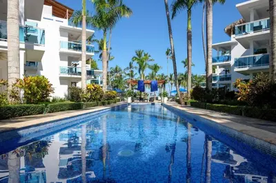 a swimming pool in front of a building with palm trees at Palmeraie Terrenas beach apartamento in Las Terrenas