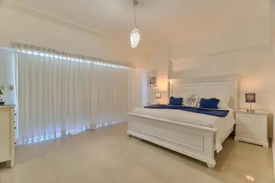 a white bedroom with a large bed with blue pillows at Sunset View 2BR Apartamento Juan Dolio Las Velas in Juan Dolio