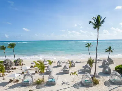 a beach with chairs and palm trees and the ocean at JOIA Bavaro by Iberostar - Adults Only All Inclusive Resort in Punta Cana