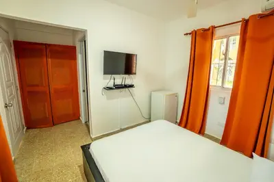 a bedroom with a bed with an orange curtain and a television at Bungalow #3 at Waterfront Playa Alicia in Sosúa