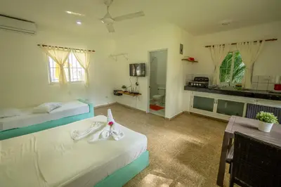 a bedroom with two beds and a table and a kitchen at Bungalow #7 at Waterfront Playa Alicia in Sosúa