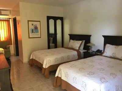 a bedroom with two beds and a living room at Hotel Las Caobas in San Francisco de Macorís
