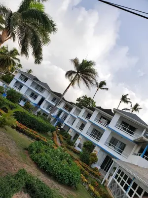 a large white building with palm trees in the background at Costarena Beach Hotel in Las Terrenas