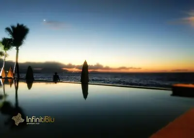 a swimming pool with a sunset in the background at Infiniti Blu Luxury Ocean Front Condos in Sosúa