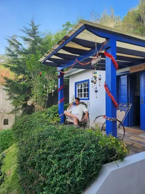 a man sitting on a porch of a blue house at Chalet los Pinos Constanza in Arroyo Frío