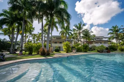 a swimming pool with palm trees in front of a building at Family Dominicus Apartment - Bayahibe in Bayahibe
