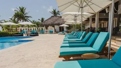 a row of blue lounge chairs next to a swimming pool at Hard Rock Golf Cozy 1BR • Pool & Golf Views in Punta Cana