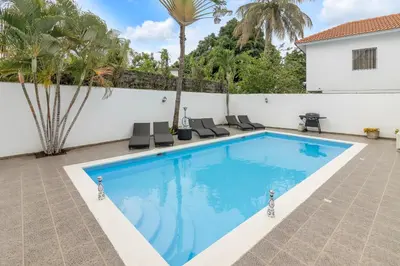 a swimming pool with a white wall and palm trees at Spacious 3BR APMT- smart speakers Airport transfer in Sosúa