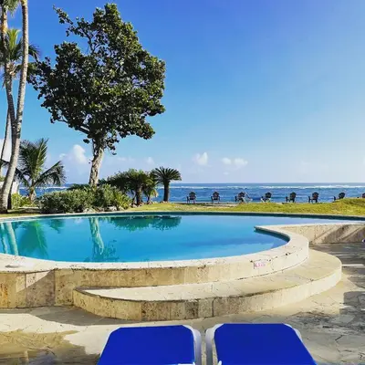 a swimming pool with two blue chairs in front of the ocean at Agualina Kite Hotel Oceanfront Apartments in Cabarete