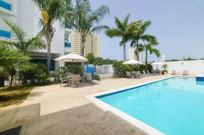 a swimming pool with chairs and umbrellas next to a building at Chic and Relax Apartamento Juan Dolio in San Pedro de Macorís