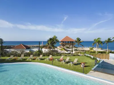 a pool with chairs and the ocean in the background at Hilton Garden Inn La Romana in La Romana