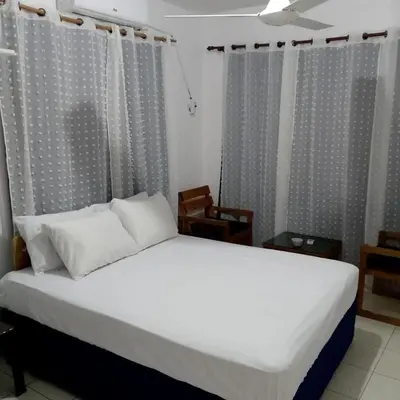 a bedroom with a bed with white sheets and curtains at Hotel Ningo in Santa Bárbara de Samaná