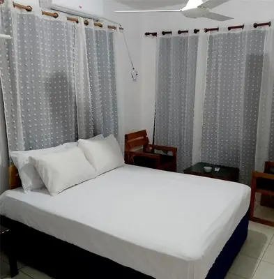 a bedroom with a bed with white sheets and curtains at Hotel Ningo in Santa Bárbara de Samaná