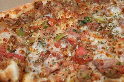 a close up of a pizza with cheese and tomatoes at Escape Penthouse near Blue Mall - 4BR with Private Rooftop & City Views in Santo Domingo