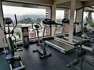 a gym with several cardio machines and windows at Paradise Room Rialto Residences in Santiago de los Caballeros
