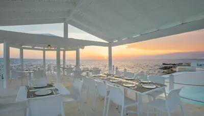 a table with white chairs and the ocean at sunset at Hotel HM Alma de Bayahibe - Adults Only - All Inclusive in Bayahibe